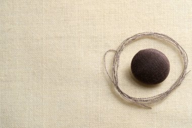 Pürüzsüz kahverengi bir düğme zarif bir şekilde yanındaki ince iplikli kumaşa bağlıdır..