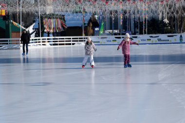 İki çocuk kış güneşinde parıldayan bir buz pateni pistinde neşeyle kayıyorlar. Kyiv, Ukrayna. 21 Şubat 2026. Ukrayna Ulusal Kompleks Expocenter, Maslenitsa