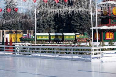 Renkli tren, pırıl pırıl dekorasyonlarla çevrili bir buz pistinin kenarında bekliyor. Kyiv, Ukrayna. 21 Şubat 2026. Ukrayna Ulusal Kompleks Expocenter, Maslenitsa