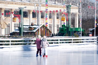 Güneşli bir günde, şenlikli bir kış buz pateni pistinde iki çocuk birlikte kayıyor. Kyiv, Ukrayna. 21 Şubat 2026. Ukrayna Ulusal Kompleks Expocenter, Maslenitsa
