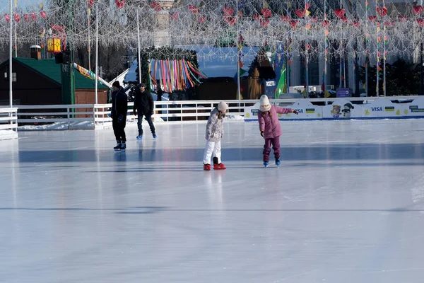 İki genç kız neşeli ışıklarla çevrili parlak bir buz pateni pistinde mutlu bir şekilde süzülüyor. Kyiv, Ukrayna. 21 Şubat 2026. Ukrayna Ulusal Kompleks Expocenter, Maslenitsa