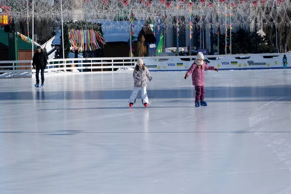 İki çocuk kış güneşinde parıldayan bir buz pateni pistinde neşeyle kayıyorlar. Kyiv, Ukrayna. 21 Şubat 2026. Ukrayna Ulusal Kompleks Expocenter, Maslenitsa
