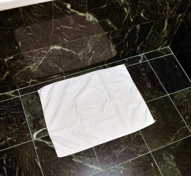 Banyodaki fayans zemininde beyaz bir ayak havlusu var..