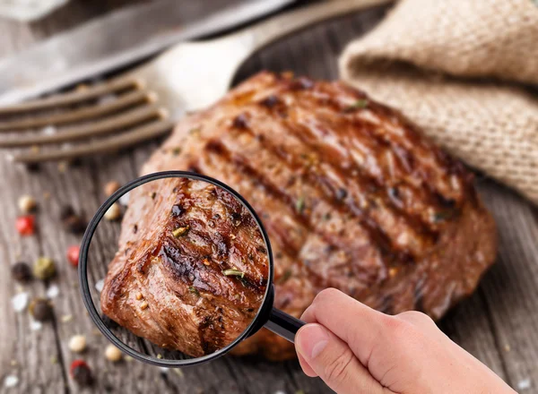 Magnifying glass examining beef steak — Stock Photo, Image