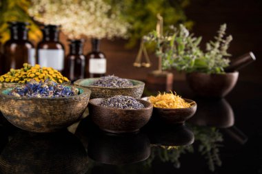 Homeopati, ahşap masada bitkisel ilaçlar, siyah ayna arka planı.