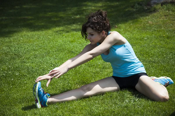 Woman stretching seated on green grass — Stock Photo, Image