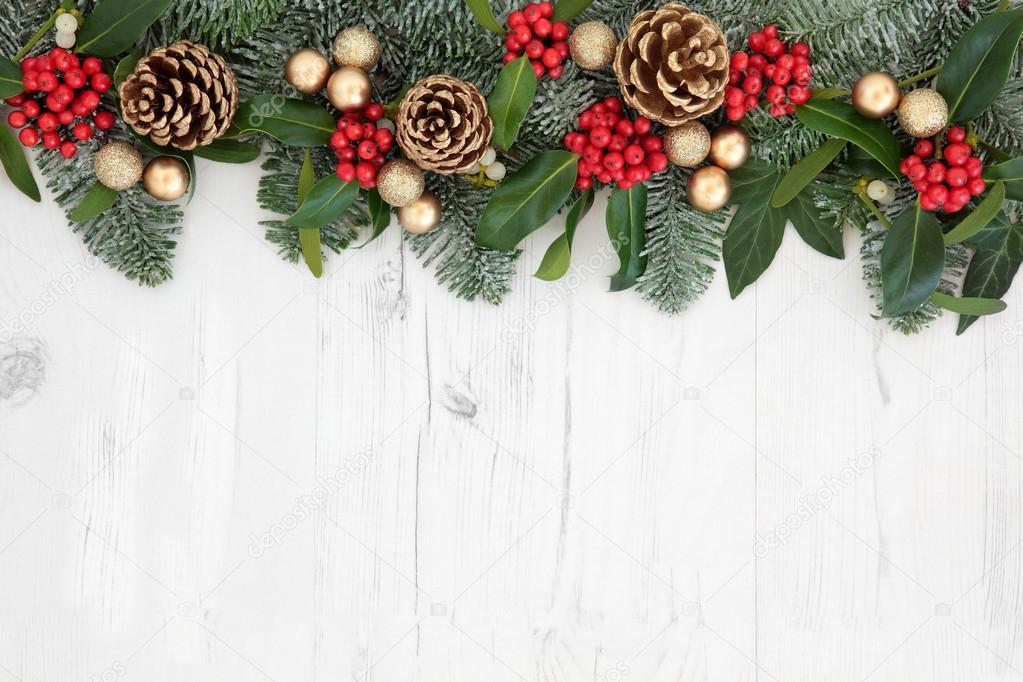 Old fashioned christmas background border with holly, mistletoe, ivy,  juniper fir and pine cones on parchment paper over old oak wood. Stock  Photo