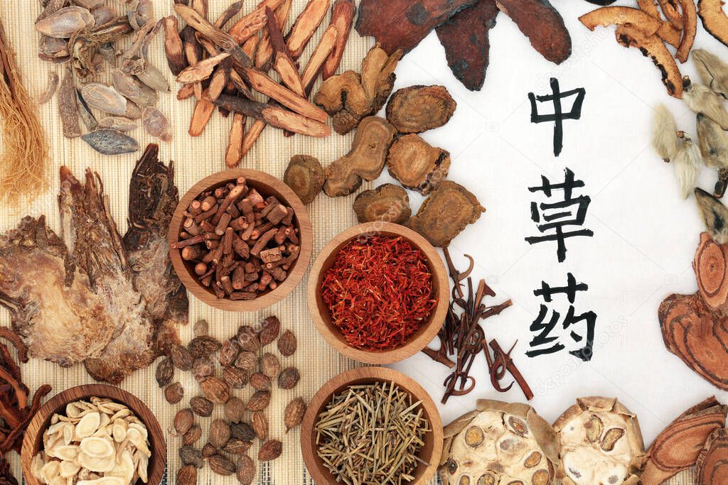 Traditional Chinese herbal medicine with herbs & calligraphy script on rice paper & bamboo. Holistic health care concept. Flat lay, top view. Translation reads as Chinese healing herbs.