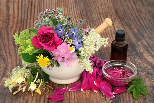 Aromatherapy essential oil preparation for herbal plant medicine treatments. Herbs and flowers in a mortar, loose and steeping in a bowl of oil. Natural plant based health care concept.