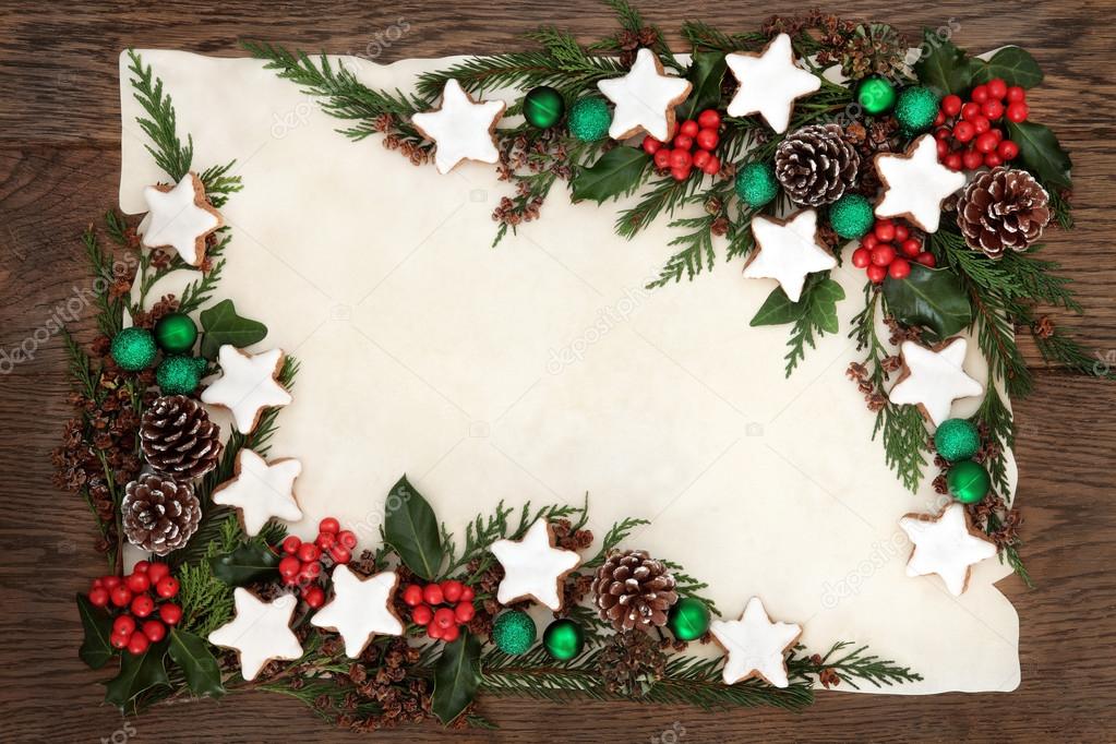 Christmas background border with poinsettia flower on parchment paper with  red and gold bauble decorations, holly, mistletoe, ivy, fir and pine cones  on oak Stock Photo