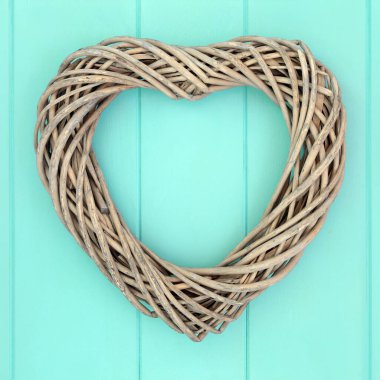 Doğal kalp şeklinde hasır çelenk. Ahşap turkuaz arka planda romantik bir dekorasyon. Aşkın sembolü.