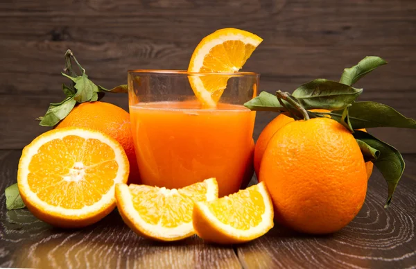 Glass of fresh orange juice and oranges on wooden background — Stock Photo, Image