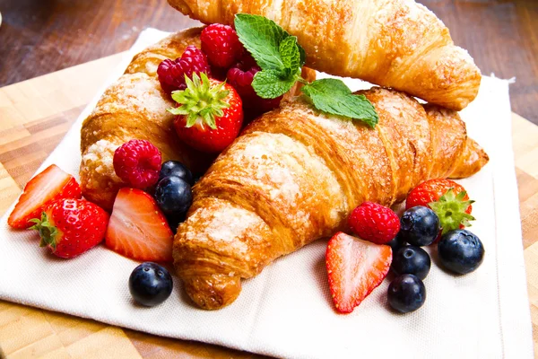 Fresh tasty croissants with berries on wooden background — Stock Photo, Image