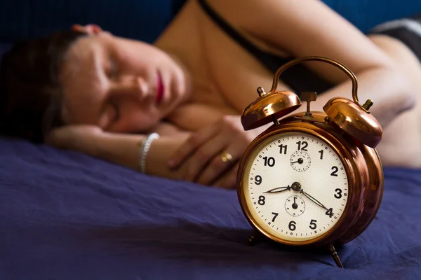 Reloj despertador en mesa y mujer durmiendo en segundo plano —  Fotos de Stock