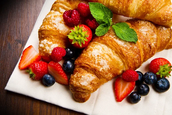 Fresh tasty croissants with berries on wooden background — Stock Photo, Image