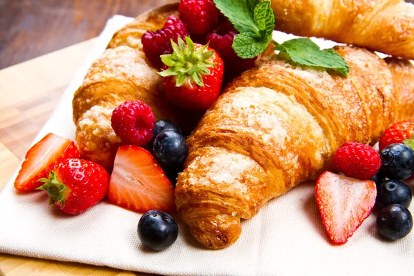Fresh tasty croissants with berries on wooden background — Stock Photo, Image