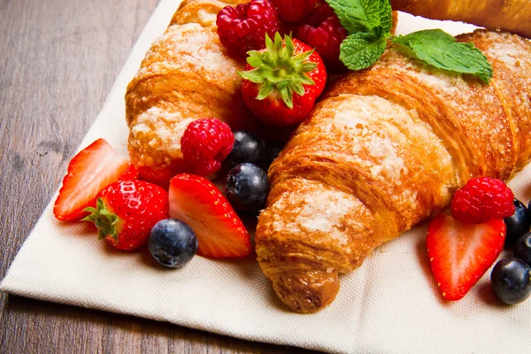 Fresh tasty croissants with berries on wooden background — Stock Photo, Image