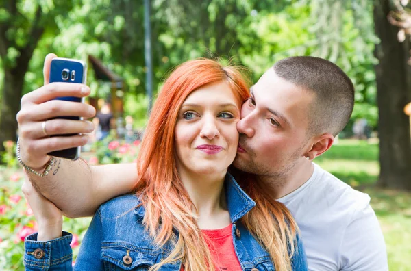 Pareja joven en un parque tomando fotos de sí mismos — Foto de Stock