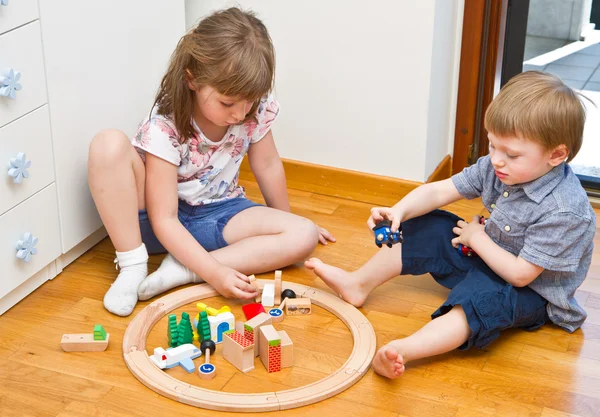 Little Children playing with wooden train in the room — Stock Photo, Image