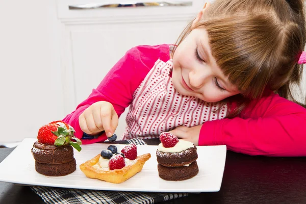 Lilla flickan förbereder och äta kakan med frukt — Stockfoto