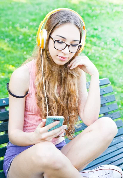 Krásné teenger naslouchat hudba sedí na lavičce — Stock fotografie