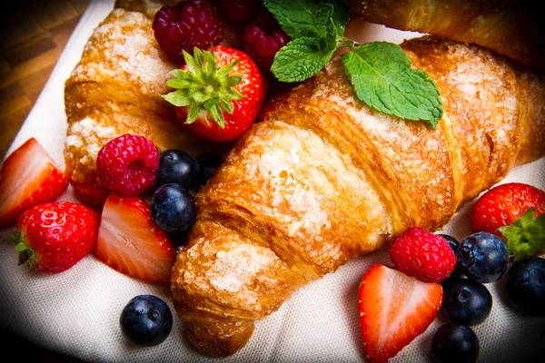 Fresh tasty croissants with berries on wooden background — Stock Photo, Image