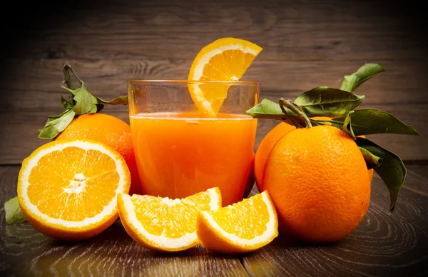 Sklenice čerstvé pomerančové šťávy a pomeranče na dřevěné pozadí — Stock fotografie