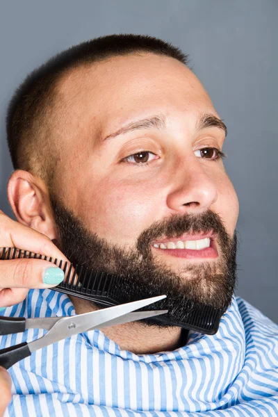 Mujer está cortando la barba de un hombre joven — Foto de Stock