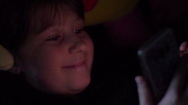 Genç kız gece yatakta akıllı telefonu izliyor.