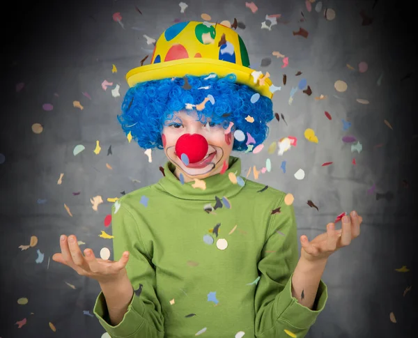 stock image young child dressed as a clown with wig and fake nose has fun playing with colorful confetti celebrating carnival