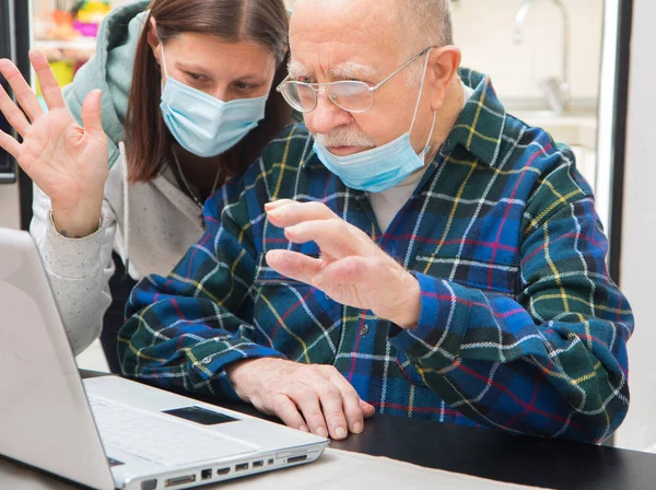 在科罗纳维勒斯潘德米亚期间 老人和他的看护者正在家里用笔记本电脑做一个视频 — 图库照片