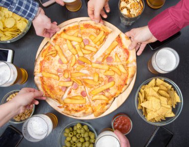 Bir grup arkadaş evde dinlenirken bira içiyor, pizza yiyor, konuşuyor ve gülümsüyor.