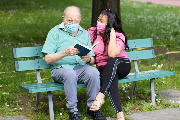 上了年纪的病人和他的照顾者一起拿着一本书看书 在一起消磨时光 — 图库照片