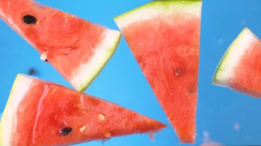 Mavi arka planda suya düşen karpuz dilimleri.