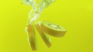 Kivi meyvesi dilimleri yavaş çekimde suya düşer.