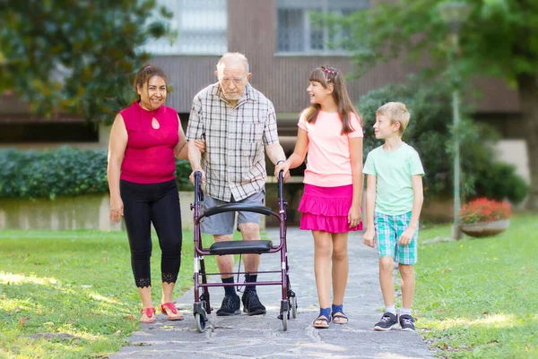 孙子孙女和保姆陪他们的祖父散步帮助他 — 图库照片
