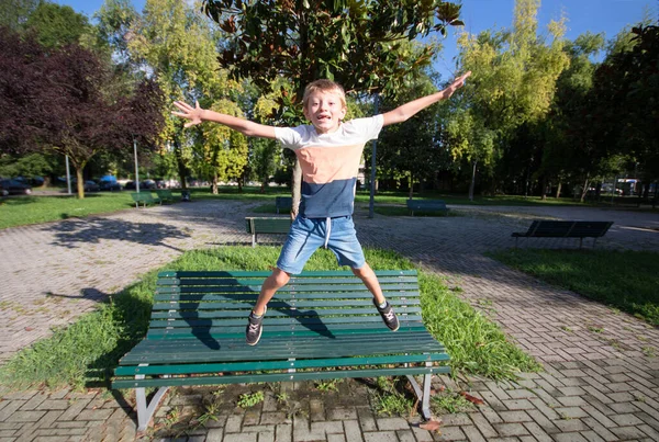 Niño Feliz Divierte Saltando Desde Banco Parque —  Fotos de Stock