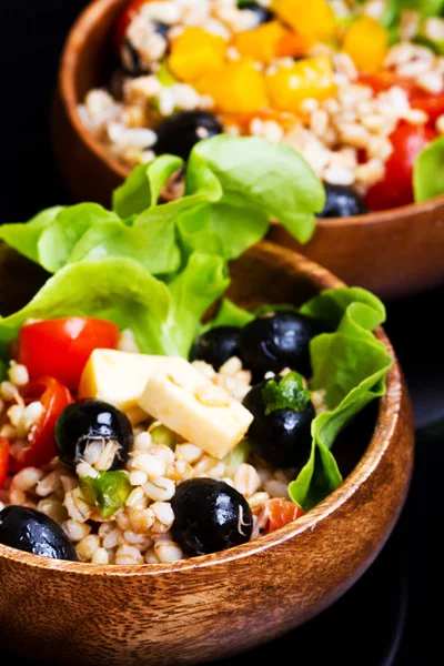 Wood bowl with spelt salad with olives and tomatoes — Stock Photo, Image
