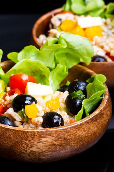Wood bowl with spelt salad with olives and tomatoes — Stock Photo, Image