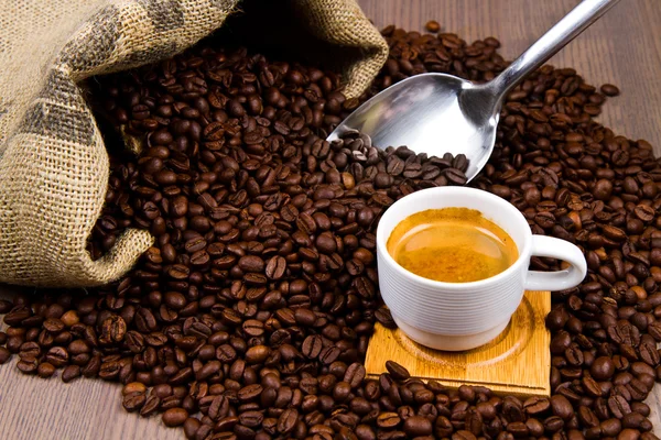 Koffiekopje met jute zak van geroosterde bonen op rustieke tabel — Stockfoto