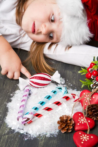Menina engraçada em chapéu de Santa escreve carta para Papai Noel perto de decoração de Natal — Fotografia de Stock
