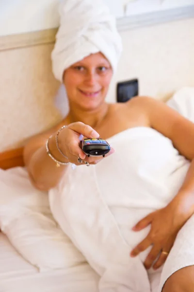 Hermosa joven mujer viendo televisión sentado en la cama con el control remoto en su mano — Foto de Stock
