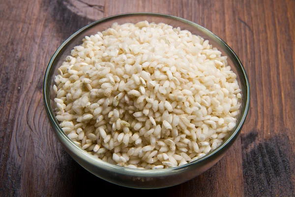 Ahşap masa üzerinde ahşap kase çiğ pirinç — Stok fotoğraf