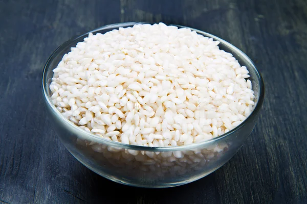 Ahşap masa üzerinde cam kapta çiğ pirinç — Stok fotoğraf