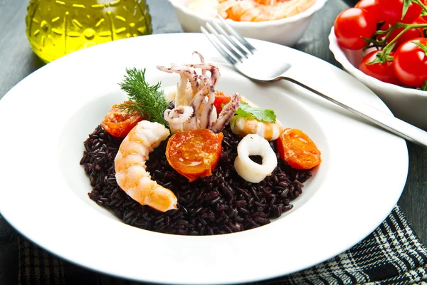 Zwarte rijst met gesneden inktvis, garnalen en tomaat op witte plaat — Stockfoto