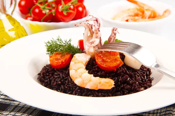 Black rice with sliced squids ,prawns and tomato on white plate Stock