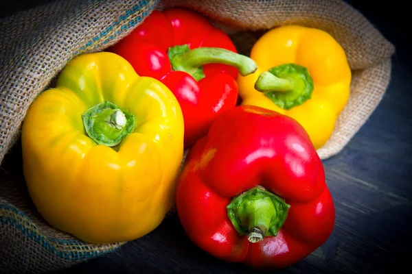 Red and yellow pepper on burlap sack on wooden — Stock Photo, Image