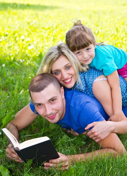 Doce família lendo um livro na grama verde — Fotografia de Stock