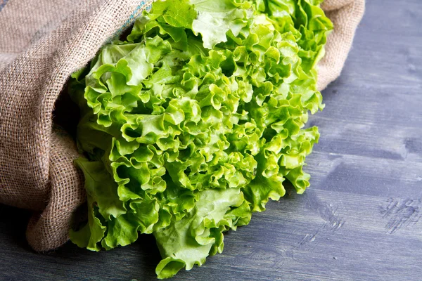 Fräsch sallad i säckväv säck på trä — Stockfoto