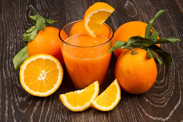 Vidro de suco de laranja fresco e laranjas no fundo de madeira — Fotografia de Stock
